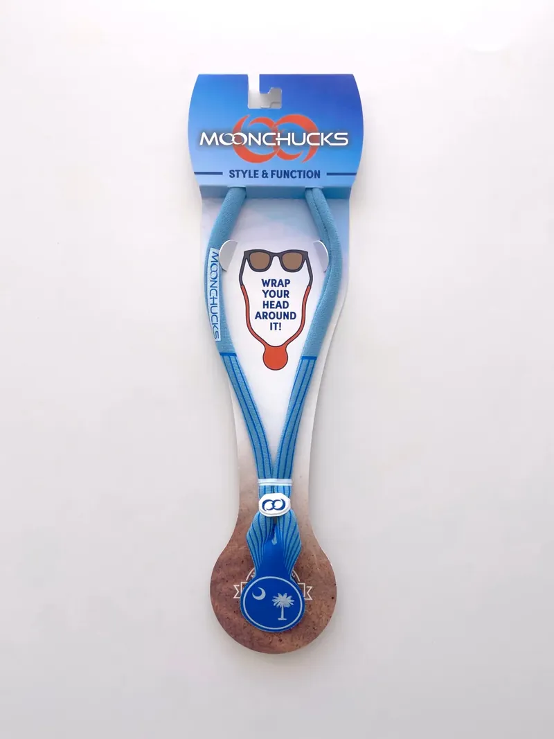 Light blue neoprene sunglass cord on its retail card, a loop of cord with a blue round badge showing a white palmetto and crescent moon at the bottom, under the Moonchucks logo and 'Wrap your head around it!'.