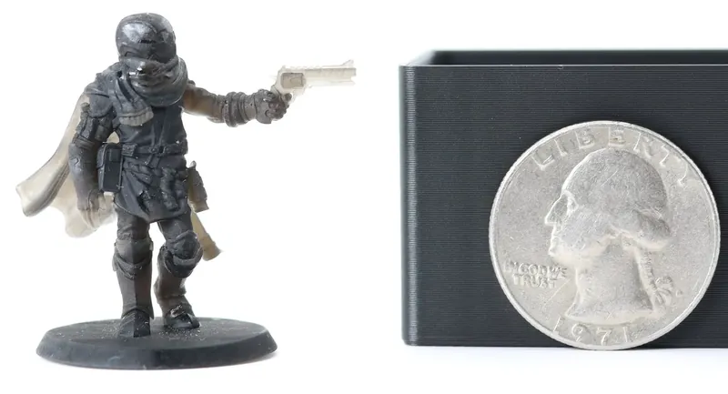 Finely detailed dark miniature, printed by us in resin, of a caped sci-fi gunslinger aiming a pistol, shown beside a US quarter for scale.