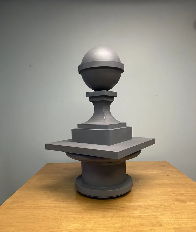 Gray 3D printed decorative post cap finial with a ball top, square knop, stepped square base and round pedestal, shown on a table.