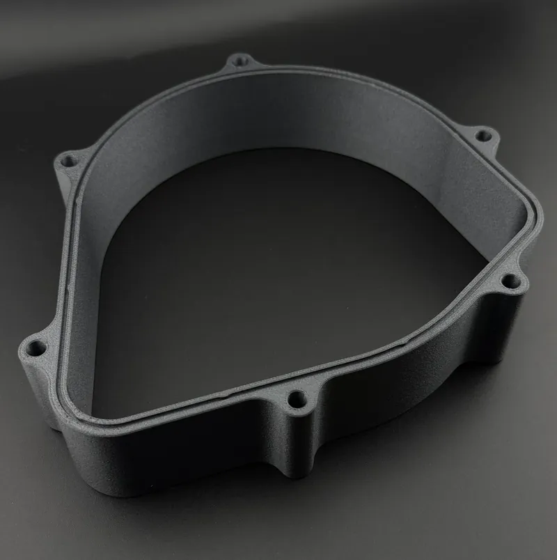 Dirt bike engine cover spacer, 3D printed in dark gray: a frame with bolt bosses around its edge and a stepped rim on its top face.