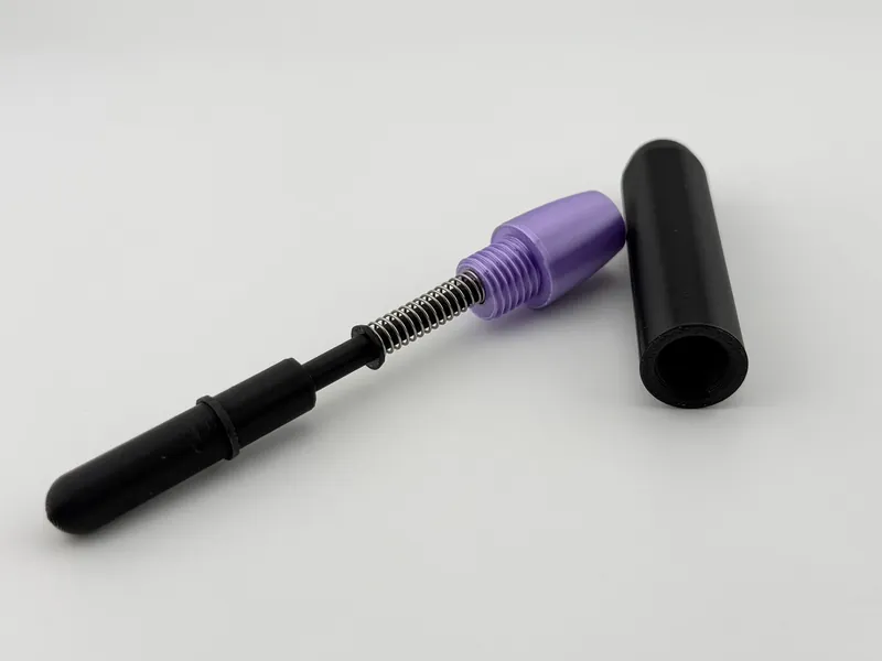 Parts of a hair braiding device, laid out as separate pieces: a black rod with a coil spring, a purple tapered cap with an external thread, and a black tube.
